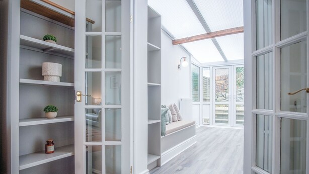 A modern interior with white shelving, a bench with cushions, and a glass door leading to an outdoor area. - Castle Square - 2 Bedroom - Mumbles (Swansea)