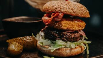 A burger with a sesame seed bun, bacon, and pickles on a plate.