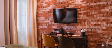 Habitación de hotel con pared de ladrillo, televisor de pantalla plana, escritorio con silla, cama y ventana con cortinas.