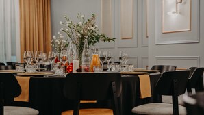 Comedor con mesas redondas dispuestas para una comida, con cristalería transparente y un centro de mesa con flores.