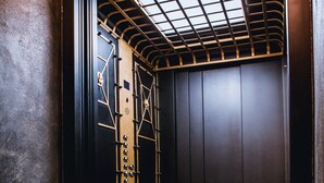 Una habitación con piso de madera, una puerta negra con celosía metálica y un tragaluz en el techo.