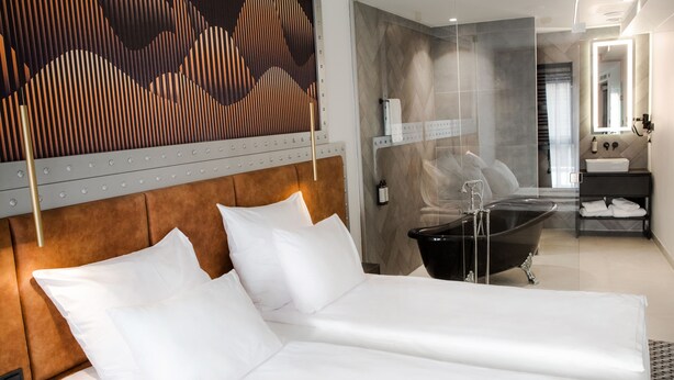 Una habitación de hotel moderna con una cama grande, una bañera y un baño con espejo y lavabo.
