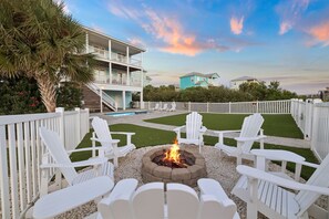 A backyard with a fire pit surrounded by white Adirondack chairs, a pool, and a two-story building in the background. - Pet-Friendly Retreat with Pool (Cape San Blas)