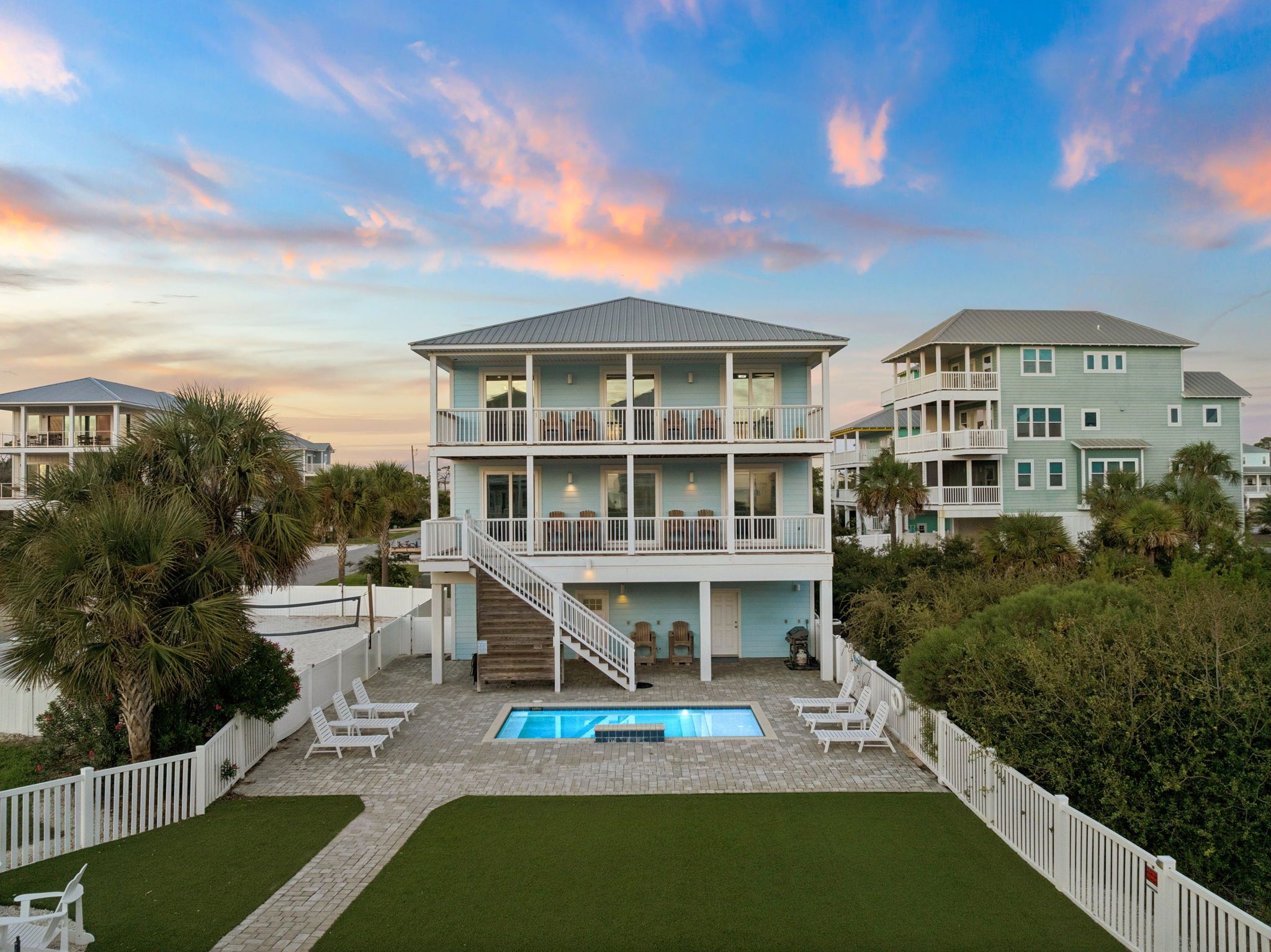 A multi-story beachfront property with a swimming pool, outdoor seating, and a staircase leading to the upper levels.