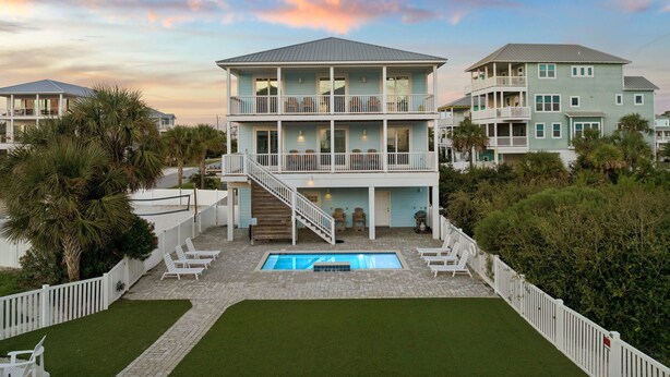 A multi-story beachfront property with a swimming pool, outdoor seating, and a staircase leading to the upper levels.