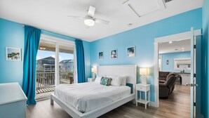 A bedroom with a bed, nightstands, a ceiling fan, and a view of a balcony.