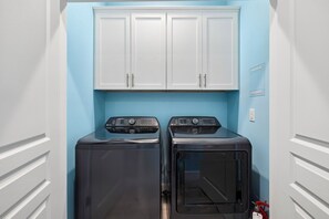 A laundry room with two front-loading washing machines and a white cabinet above. - Pet-Friendly Retreat with Pool (Cape San Blas)