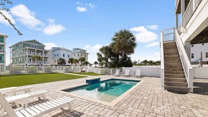 A swimming pool with a brick deck, surrounded by white lounge chairs and a white fence.