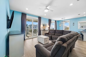 A modern living room with a sofa, a coffee table, and a TV. There is a balcony with a view of the sea. - Pet-Friendly Retreat with Pool (Cape San Blas)
