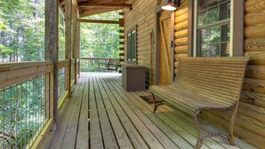 A wooden cabin with a porch, a bench, and a window.