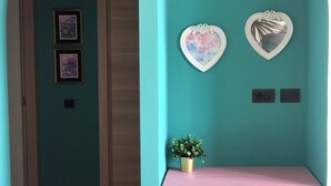 Et værelse med teal vægge, et pink bord, to hjerteformede dekorationer på væggen og en lille plantepotte.