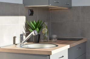 Ett modernt kök med en diskho i rostfritt stål, en aloe vera-planta i en kruka, en glasflaska och ett glas.