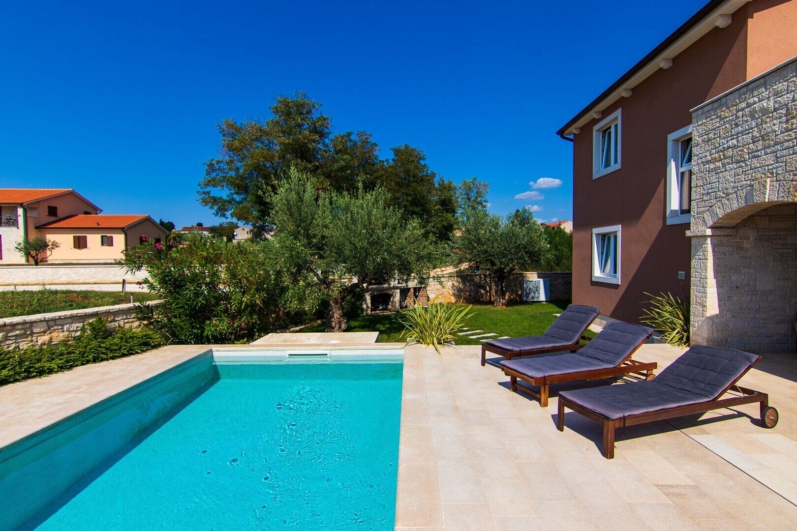 A swimming pool with two sun loungers and a stone wall.