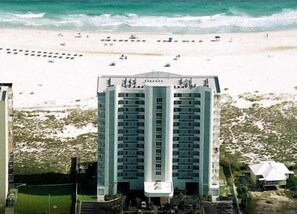 Een hoog hotel met meerdere verdiepingen, een strand op de achtergrond en een helder uitzicht op de oceaan.