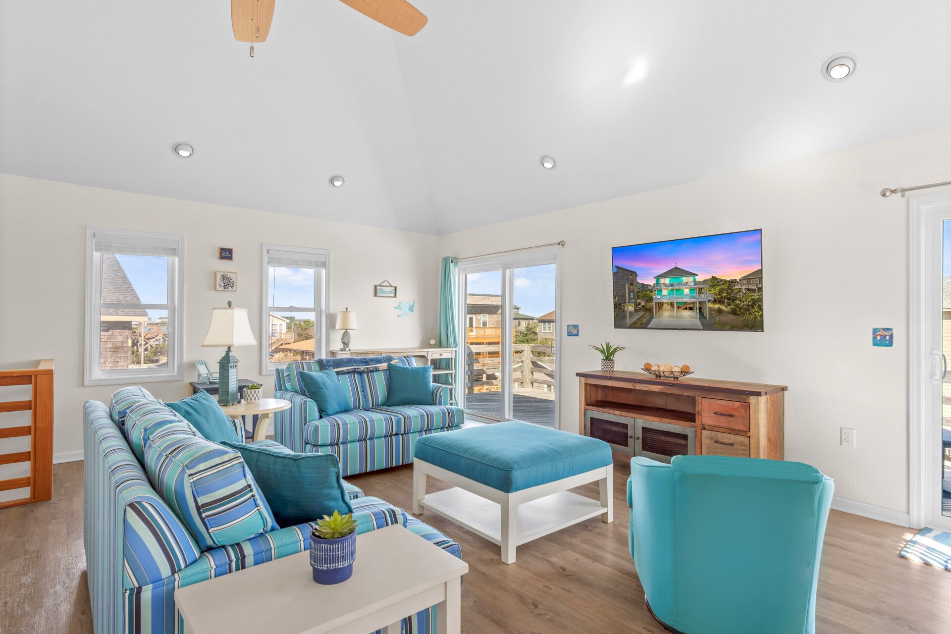 A spacious living room with striped sofas, a teal armchair, and a flat-screen TV mounted on the wall.