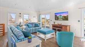 Un salon spacieux avec des canapés à rayures, un fauteuil de couleur turquoise et un téléviseur à écran plat fixé au mur.