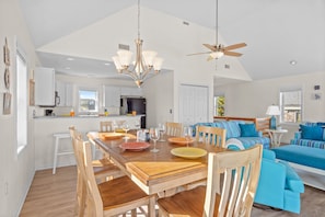 A spacious living area with a wooden dining table, blue sofa, and a ceiling fan.