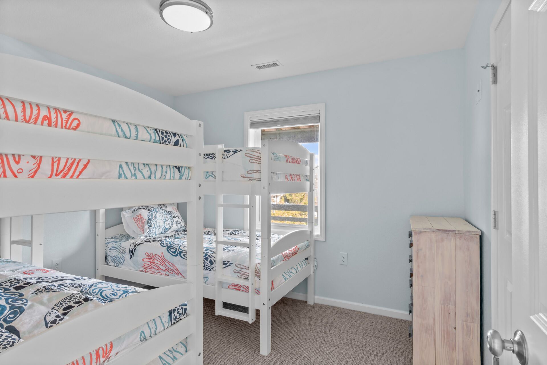 Une chambre d’enfant avec des lits superposés, une fenêtre et une armoire en bois.