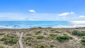 Un sentier côtier menant à la plage, bordée de dunes et d’une végétation clairsemée.