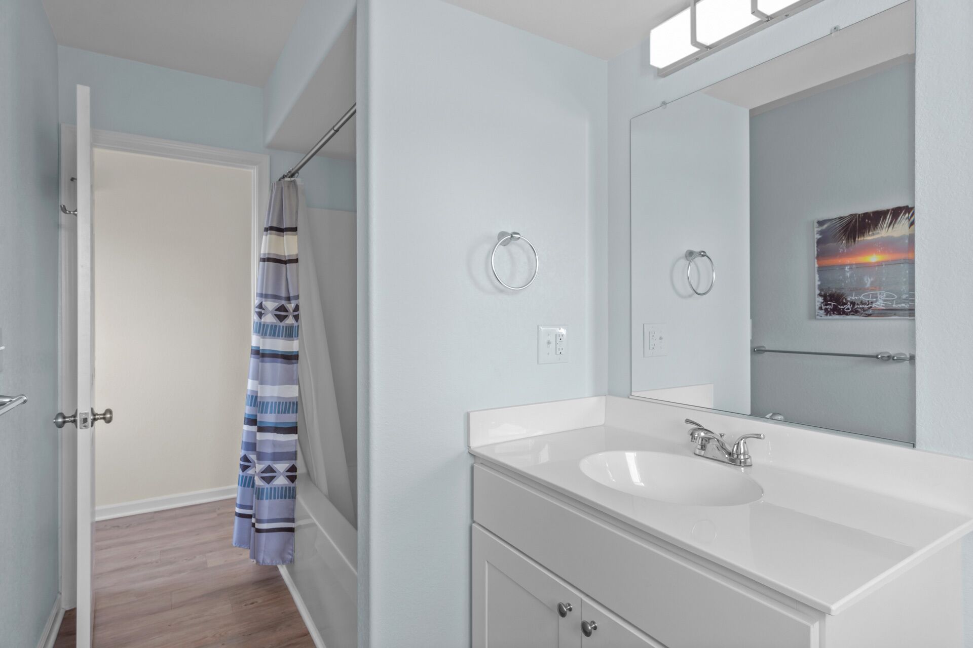 A modern bathroom with a white sink, a large mirror, and a towel ring.