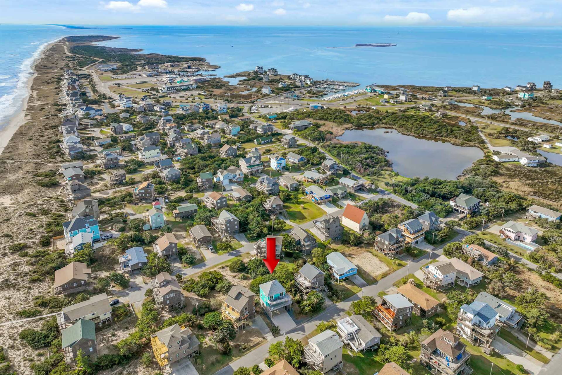 An aerial view of a coastal residential area with houses, a beach, and a marina.
