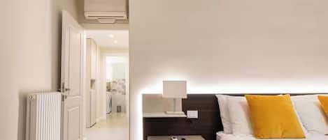 A hotel room with a bed, bedside table, lamp, and a view of the hallway.
