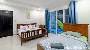 Un dormitorio con dos camas de madera, un ventanal corredizo a un balcón y una puerta negra.