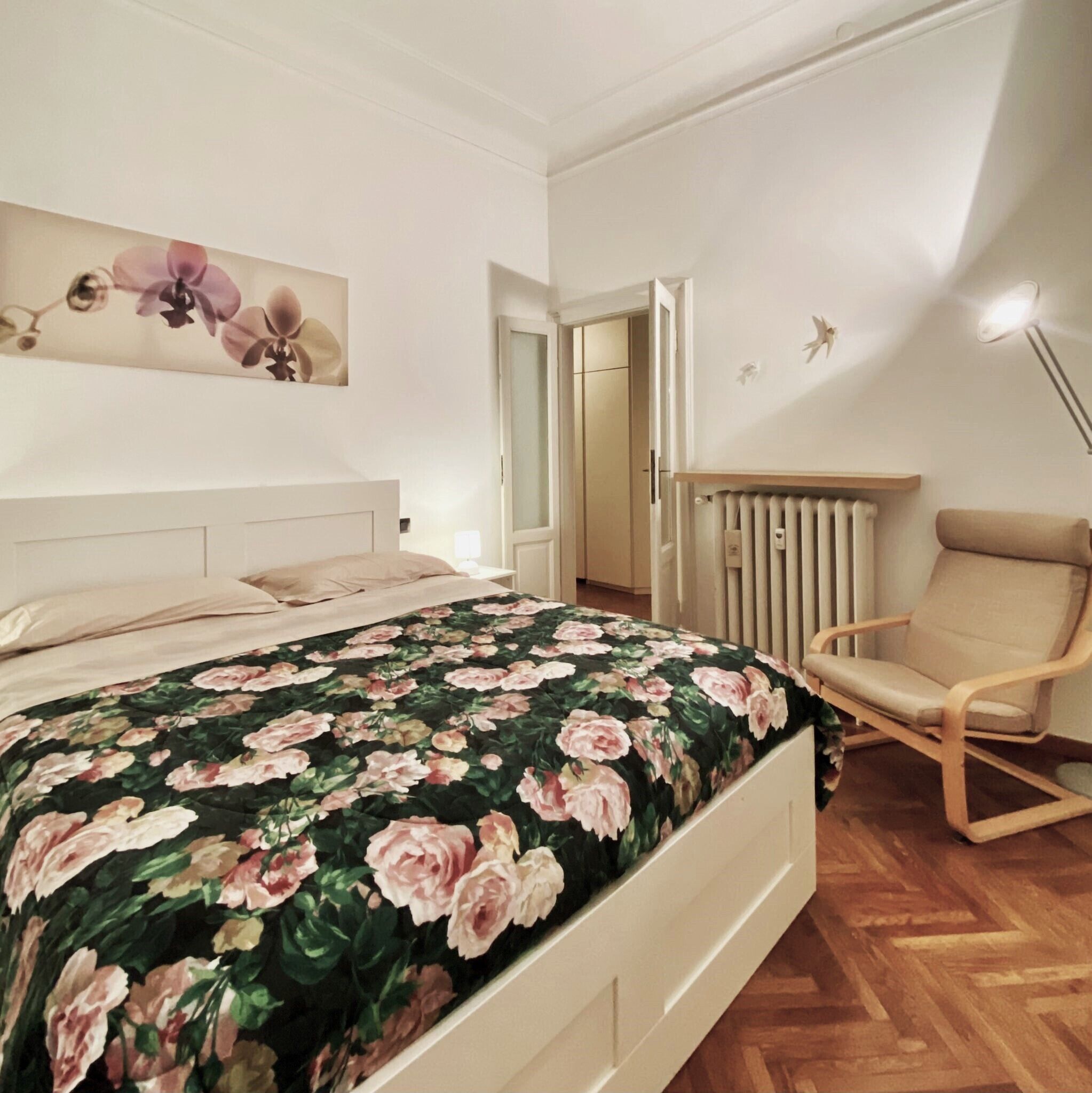 A bedroom with a bed, a chair, a radiator, and a door leading to another room.