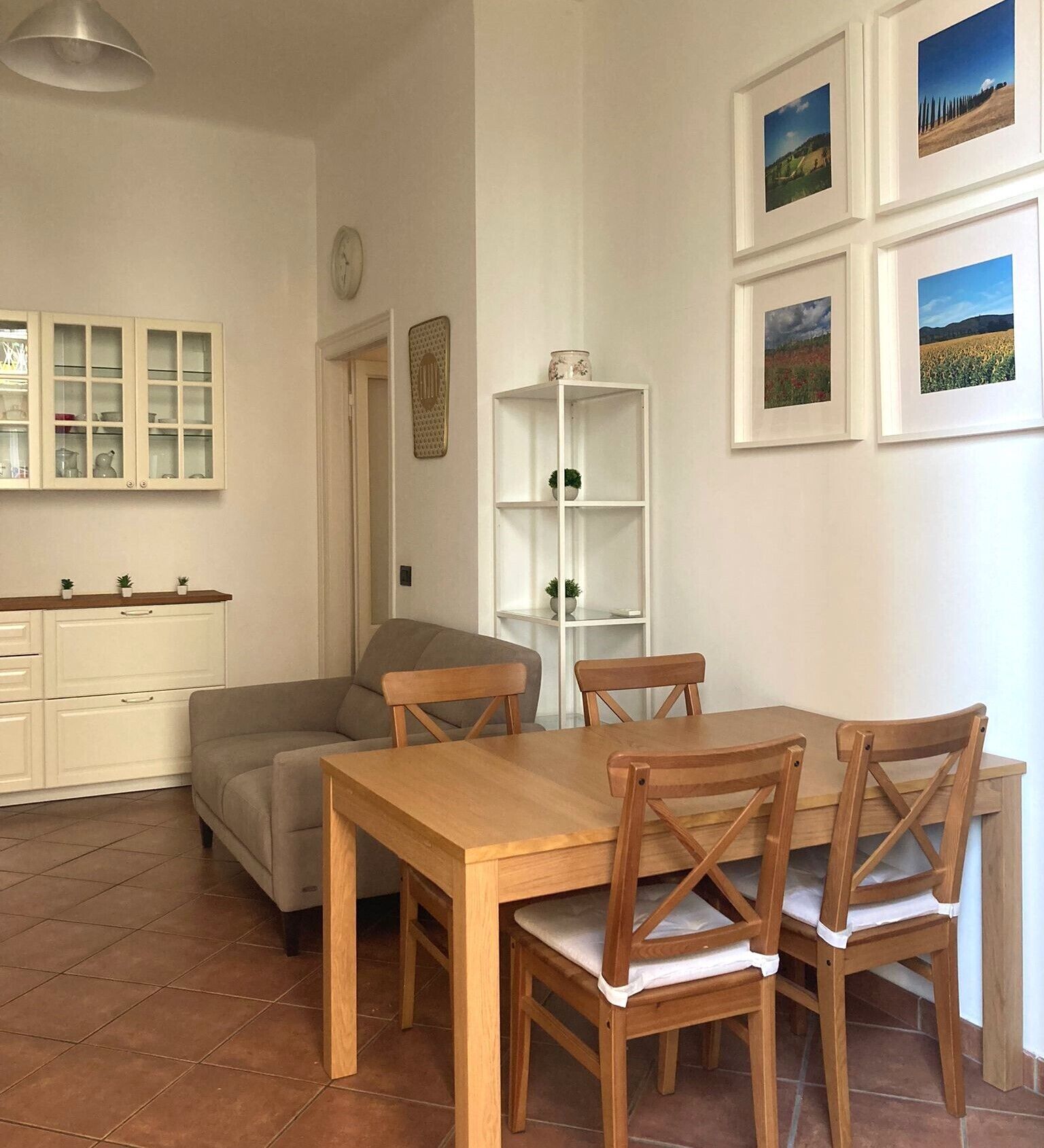 A dining area with a wooden table and chairs, a white cabinet with glass doors, and a white shelving unit.