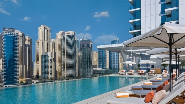 Una piscina sul tetto con sedie a sdraio e ombrelloni, con vista su un panorama urbano caratterizzato da grattacieli.