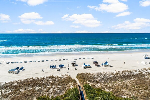 Ein Strand mit Liegestühlen, Sonnenschirmen, einem Rettungsturm und einem Sandweg, der zum Strand führt.
