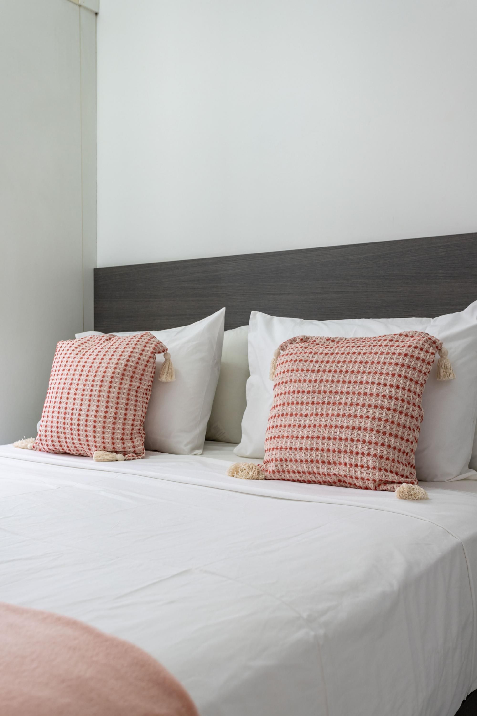 Una cama bien hecha con sábanas blancas y dos almohadas decorativas con un estampado rojo y blanco.