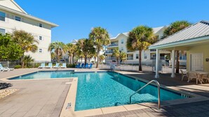 A swimming pool with lounge chairs and palm trees, surrounded by buildings with balconies. - 🌴Cute 1BR|Steps2Beach w/ Incredible View|Pool!🌴 (Navarre Beach)
