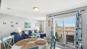 A living room with a round table, teal chairs, and a sofa set. There is a balcony with a view of the beach. - 🌴Cute 1BR|Steps2Beach w/ Incredible View|Pool!🌴 (Navarre Beach)