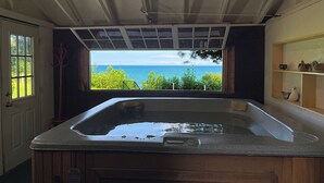 A bathroom with a large bathtub, a window with a view of the ocean, and a wooden shelf with decorative items. - Waterfront Homes in Lexington  (Lexington)