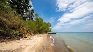 A beach with a wooden staircase leading down to the water, surrounded by trees and a clear sky. - Waterfront Homes in Lexington  (Lexington)