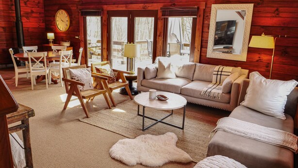 Ein gemütliches Blockhaus-Interieur mit Holzvertäfelung, einer Couch, Sesseln, einem Couchtisch und einem Kamin.
