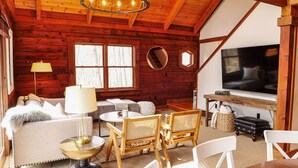 Ein gemütliches Blockhaus-Interieur mit Kamin, Fernseher und bequemen Sitzmöglichkeiten.