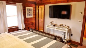 Ein Hotelzimmer mit einem Bett, einem an der Wand montierten Fernseher, einem Konsolentisch mit Dekoration und Holzwandverkleidung.