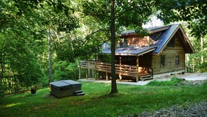 Eine Blockhütte mit einer Terrasse, umgeben von einem Wald.