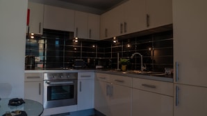 Uma cozinha moderna com eletrodomésticos de aço inoxidável, painel de azulejos pretos e iluminação pendente.