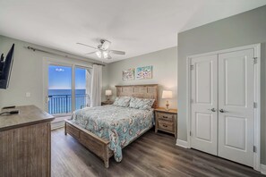 A bedroom with a bed, a desk, a ceiling fan, a nightstand, a dresser, and a door.