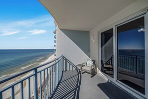 A balcony with a view of the beach and ocean, a chair, and a small table.