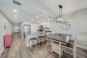 A modern kitchen with white cabinets, a central island, and a dining area with a wooden table and chairs.