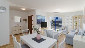 Ein modernes Wohnzimmer mit Essbereich, einem Fernseher und Blick auf die Stadt durch das Fenster.