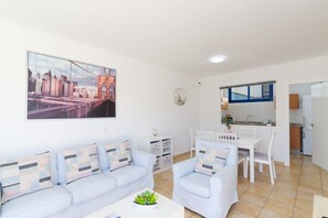 A modern living room with a sofa set, a dining table, and a kitchen area in the background.