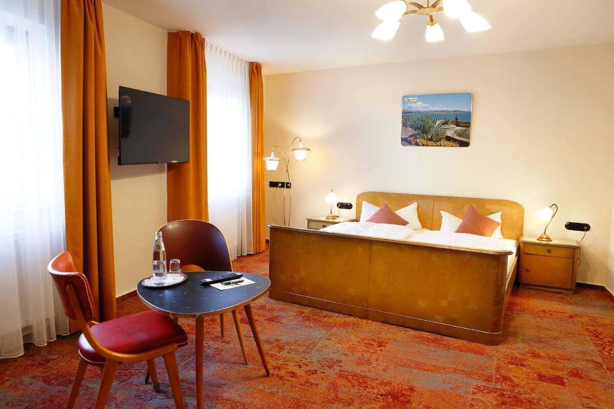 Een hotelkamer met een bed, een bureau met stoel, een aan de muur bevestigde televisie en een nachtkastje met een lamp.