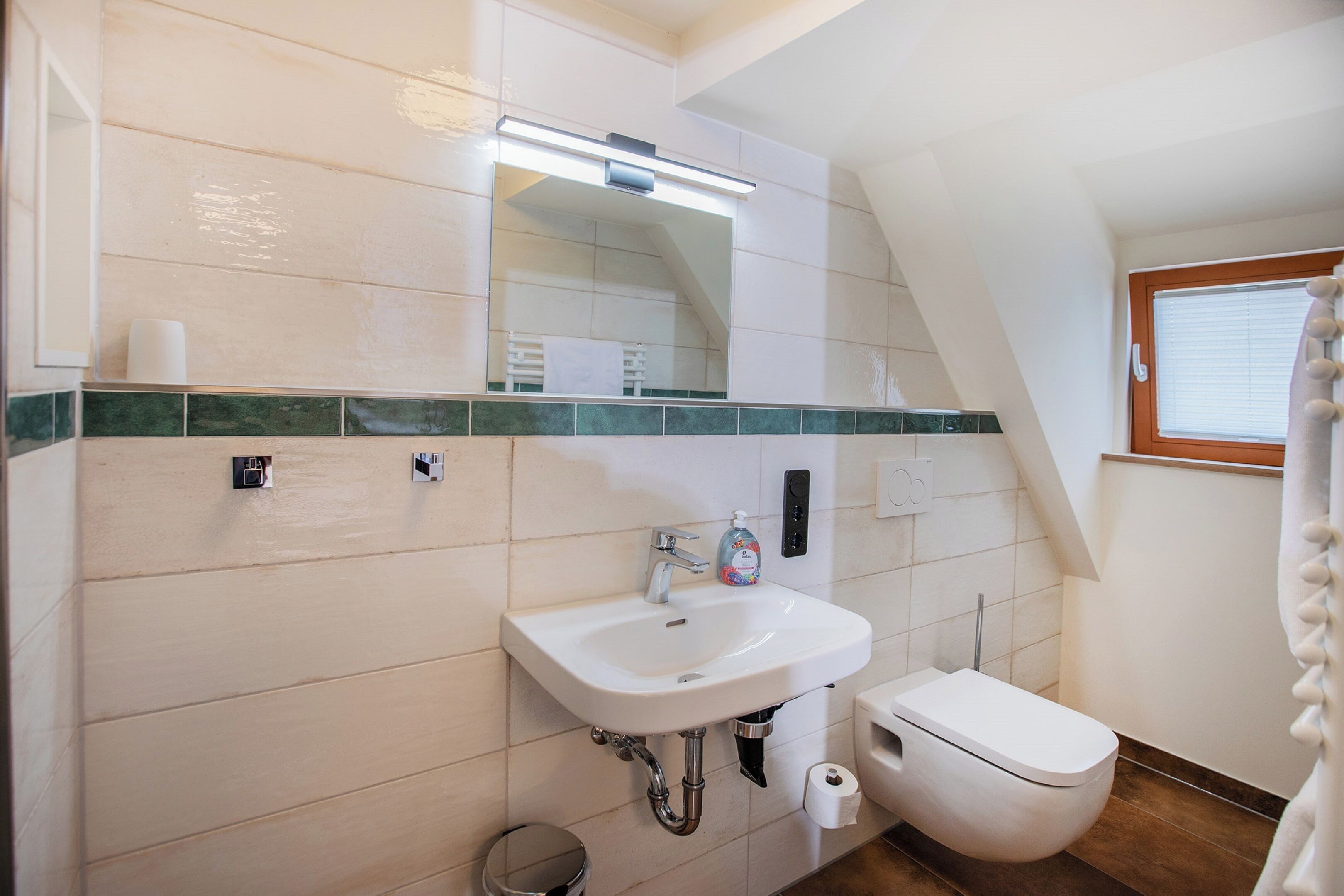 Un baño con un lavamanos blanco, un espejo, un inodoro y una ventana con cortina.