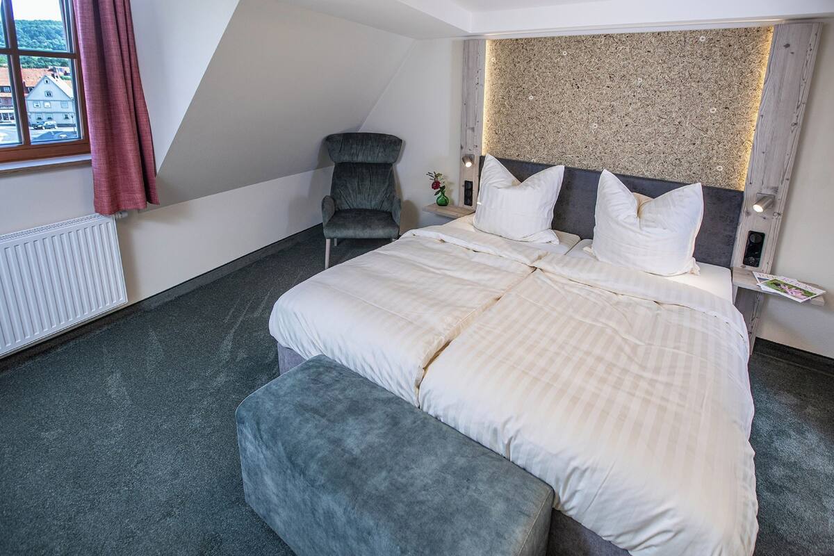 Een moderne hotelkamer met een groot bed, een grijze fauteuil en uitzicht door een raam.
