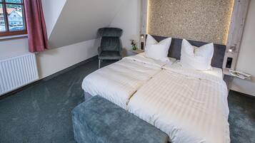 Ein modernes Hotelzimmer mit einem großen Bett, einem grauen Sessel und Blick durch ein Fenster nach draußen.